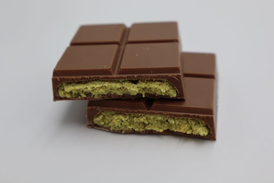A thick chocolate bar broken in half showing a bright green pistachio cream filling laced with strands of crispy toasted kataifi pastry.