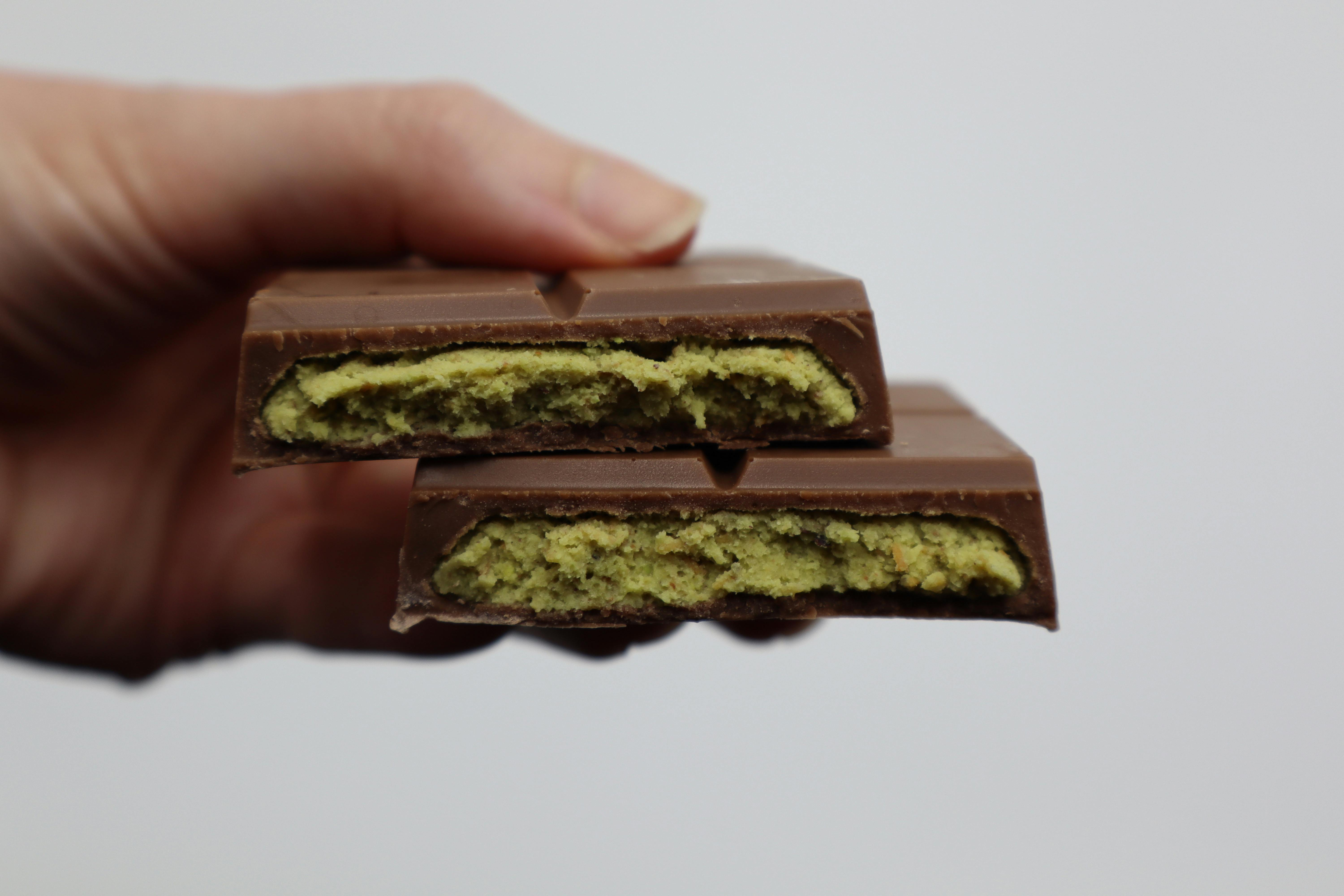 Detailed view of a milk chocolate bar with green filling held in hand against a plain background.