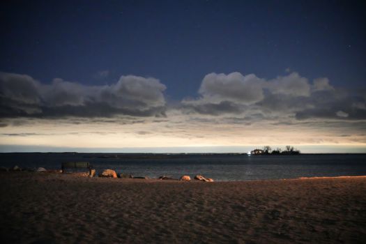 Peaceful nighttime beach with clouds and ocean horizon, hints of starlight in the sky.