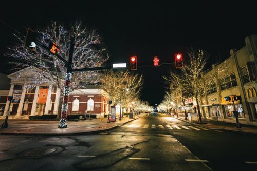 Free Empty street with festive lights illuminating buildings and trees at night. Stock Photo
