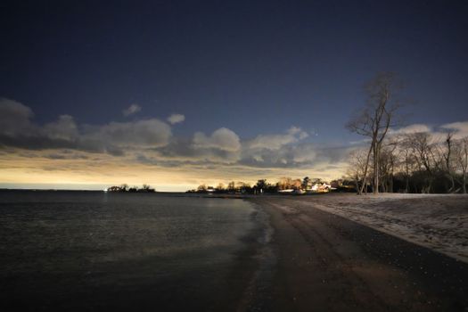 Serene nighttime beach scene with clouds and distant lights along the shoreline.