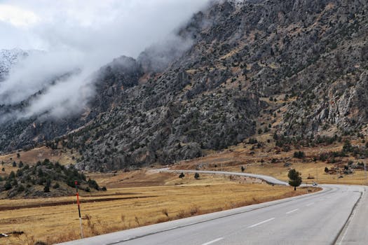Dramatic mountain landscape with a winding highway under cloudy skies.