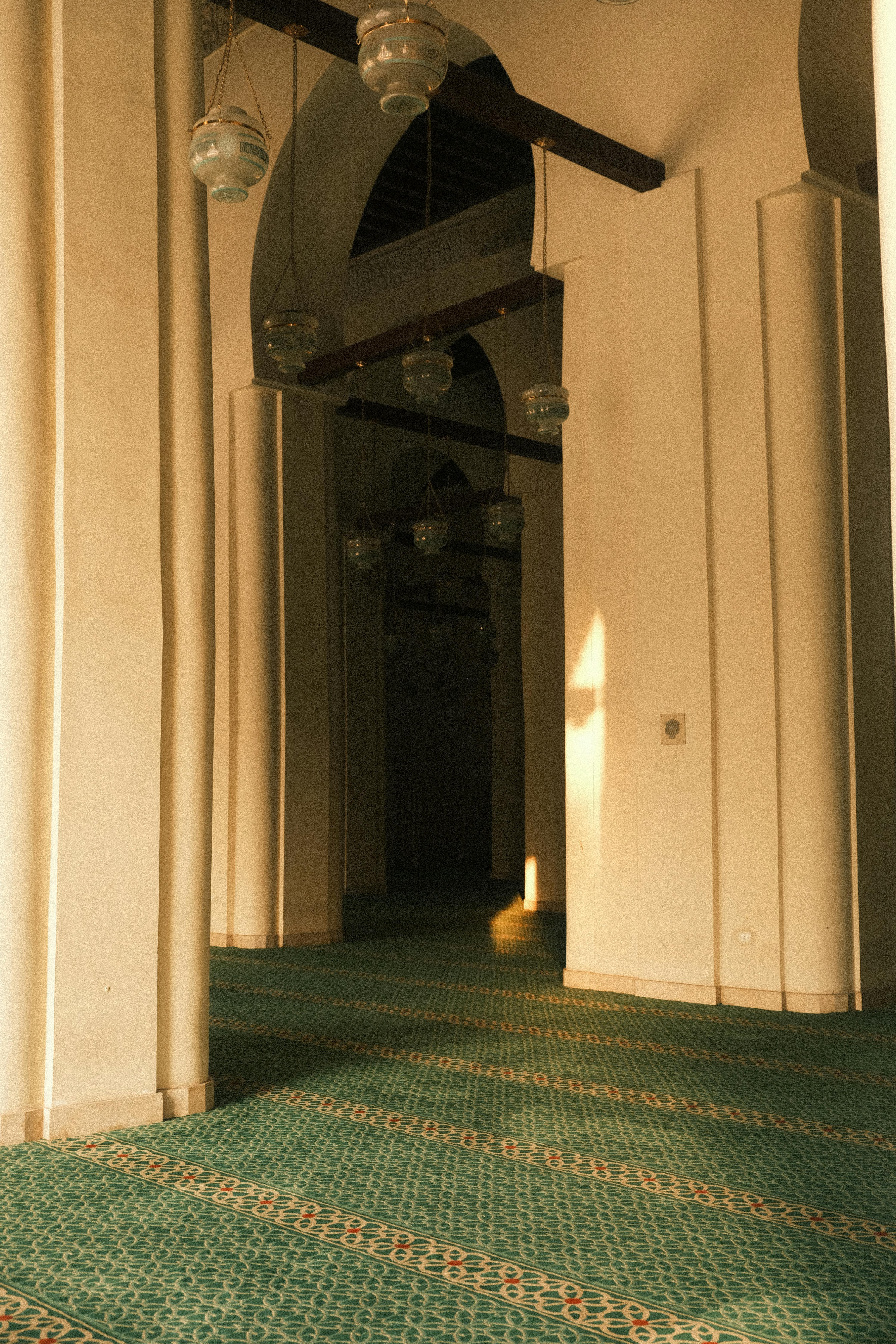 Tranquil interior view of a mosque with sunlit arches and intricate carpets.