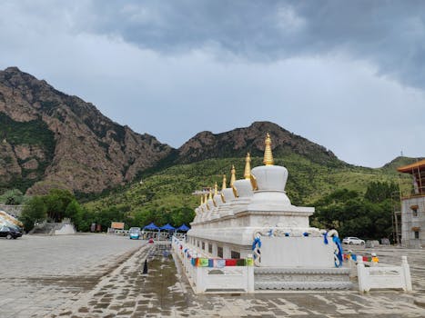 A row of stupas adorned with prayer flags at a Tibetan monastery with scenic mountain backdrop.