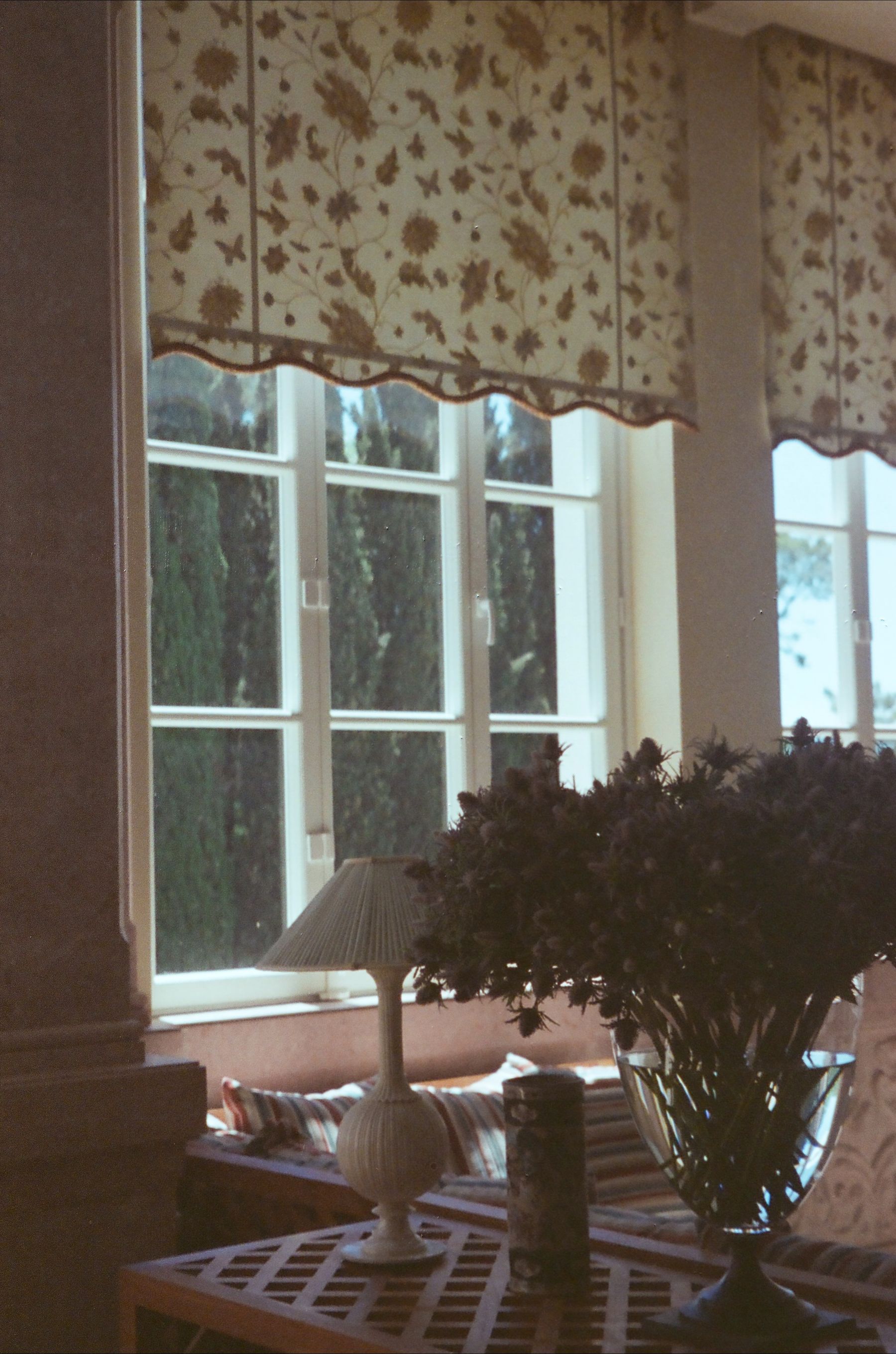 Sunlit living room with floral curtains, flowers and a warm table lamp