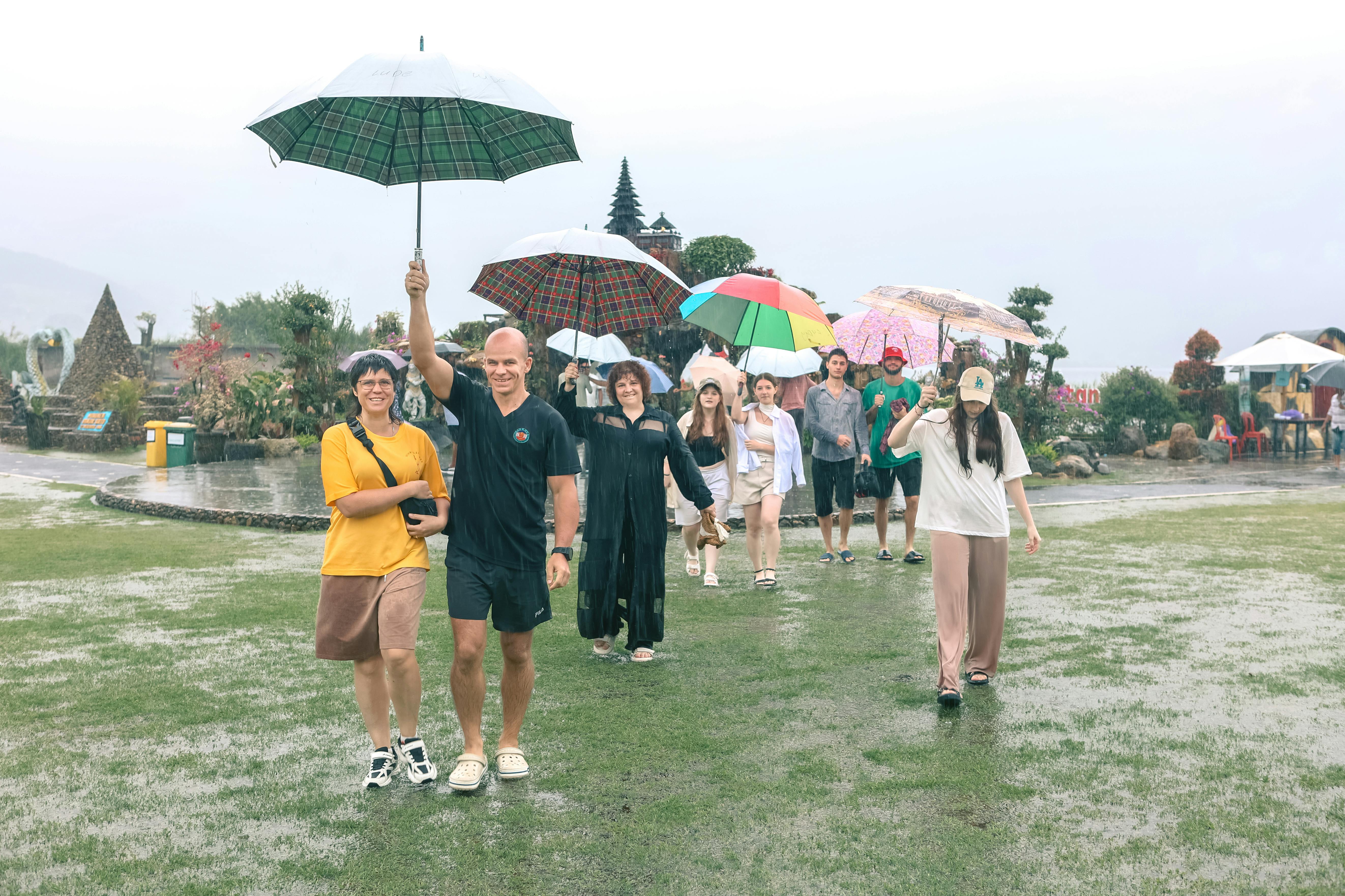 A joyful group of people walking with colorful umbrellas in a lush garden during a rainy day.