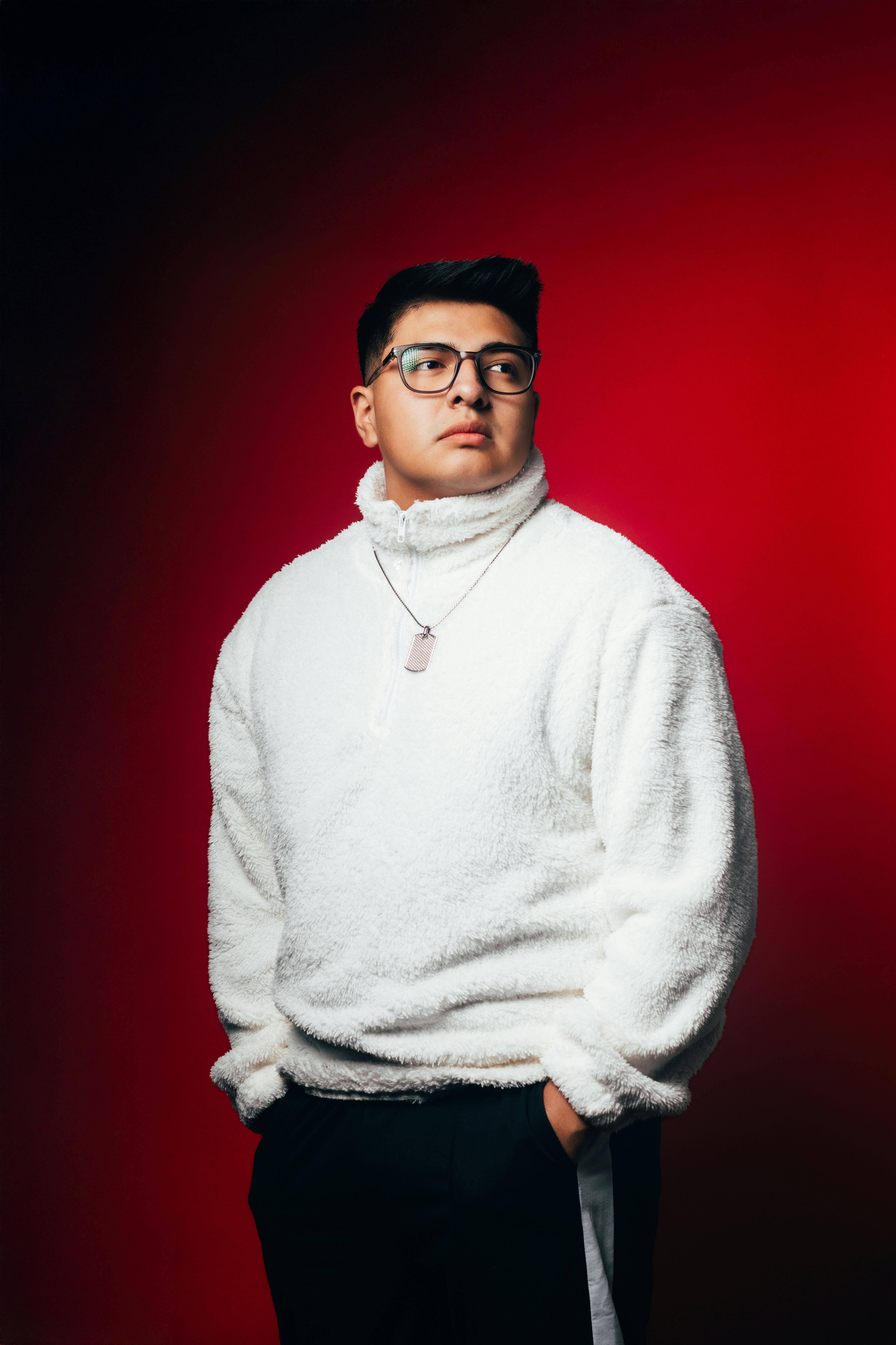 Portrait of a stylish young adult wearing a white sweater against a vibrant red backdrop.