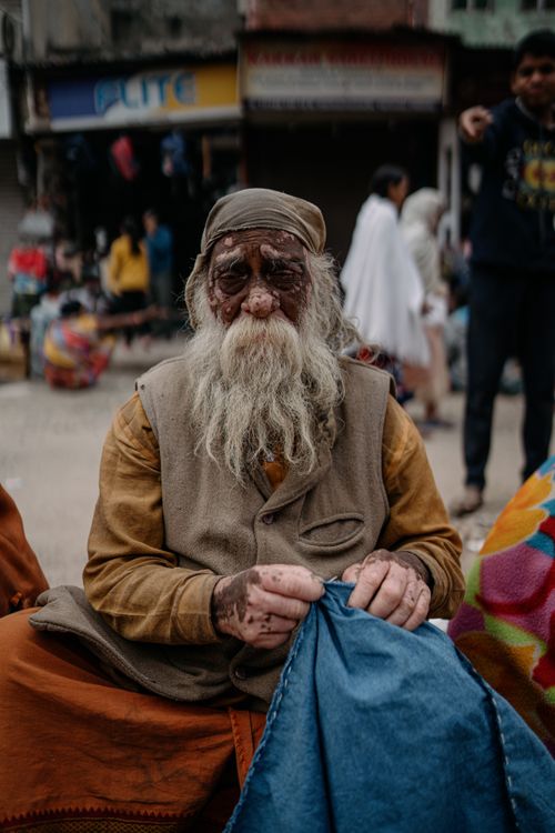 Free Portrait of a senior man in Varanasi sewing cloth outdoors, showcasing traditional Indian culture. Stock Photo