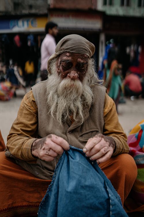 Free An elderly man with vitiligo sewing in the bustling streets of Varanasi, India. Stock Photo