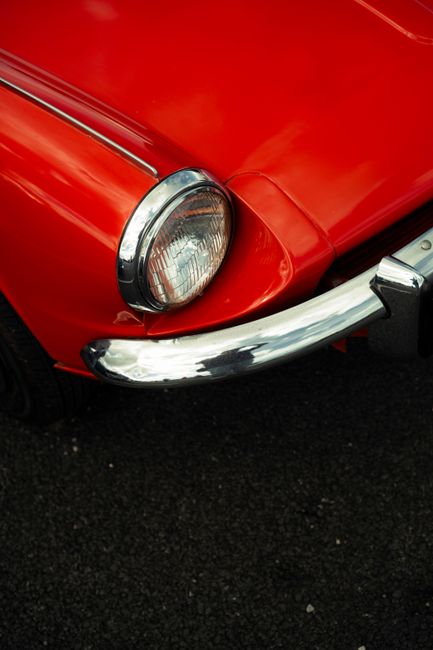 Detailed view of a classic red car's headlight and chrome bumper.