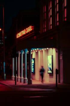A cinematic night view of a theater entrance in London with neon lights and motion blur.