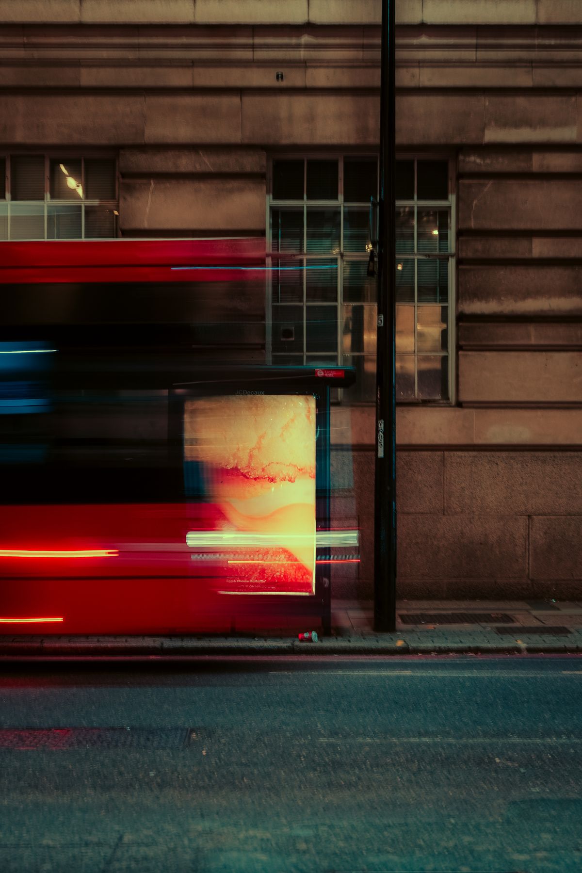 Motion-blurred red bus travelling along a city street at night