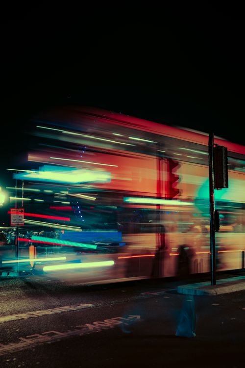 Free Dynamic long exposure of a red London bus racing through neon-lit streets at night. Stock Photo