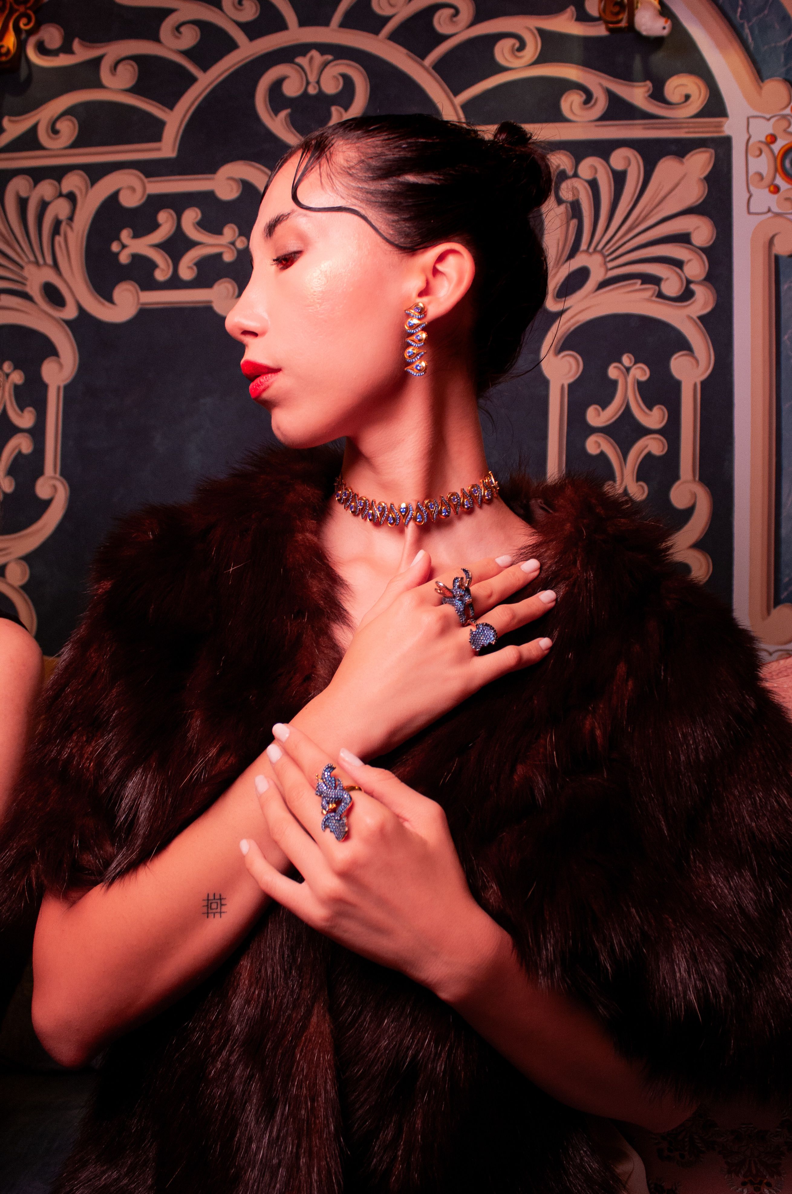 Sophisticated woman wearing exquisite jewelry and fur against ornate background.