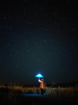 An enchanting scene of a person holding a glowing umbrella under a starlit sky.