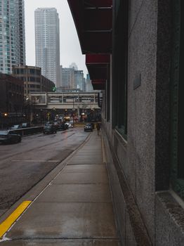 A rainy urban street with skyscrapers and traffic in downtown city during an overcast day.