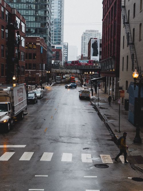 Free Damp city street with cars and people, featuring urban architecture and tall buildings. Stock Photo