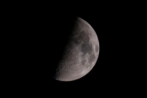 Free Stunning close-up image of the first quarter moon against a clear black sky, highlighting lunar features. Stock Photo