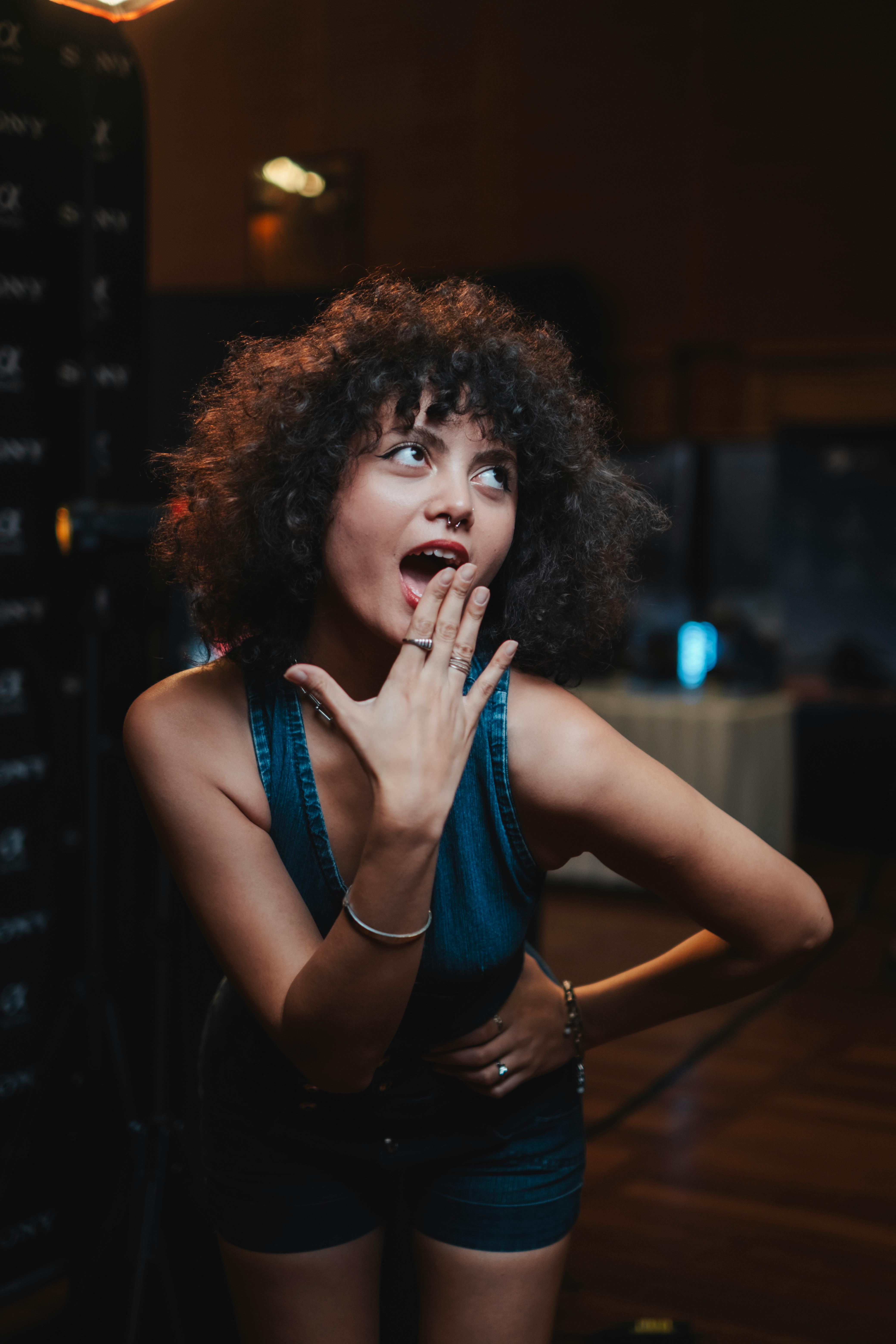 grátis Jovem mulher alegre posando em ambiente interno com gestos expressivos e cabelos cacheados. Foto profissional