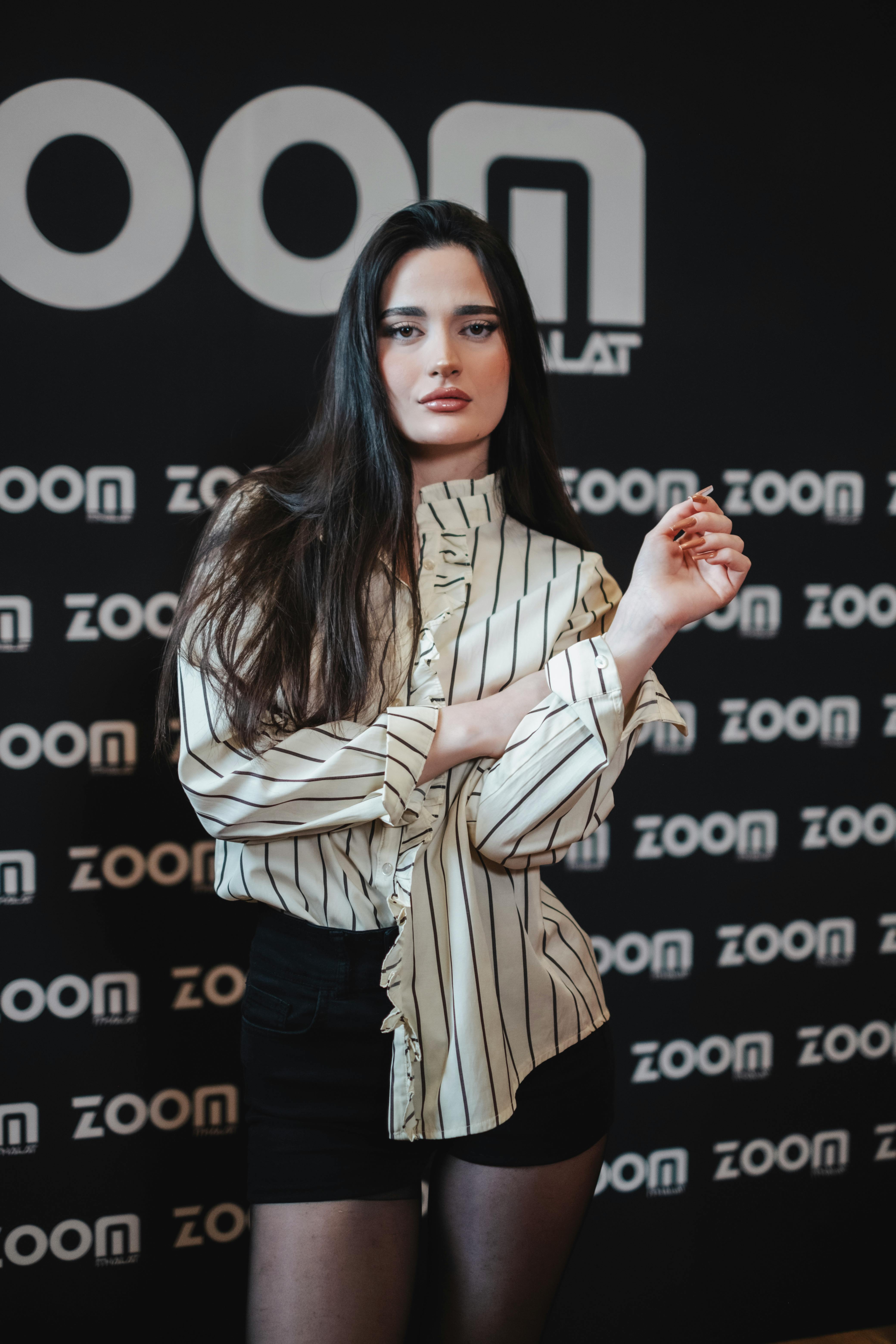 Stylish woman in striped blouse posing against Zoom-branded backdrop.