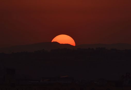A dramatic sunset with a bright orange sun setting over silhouetted hills.