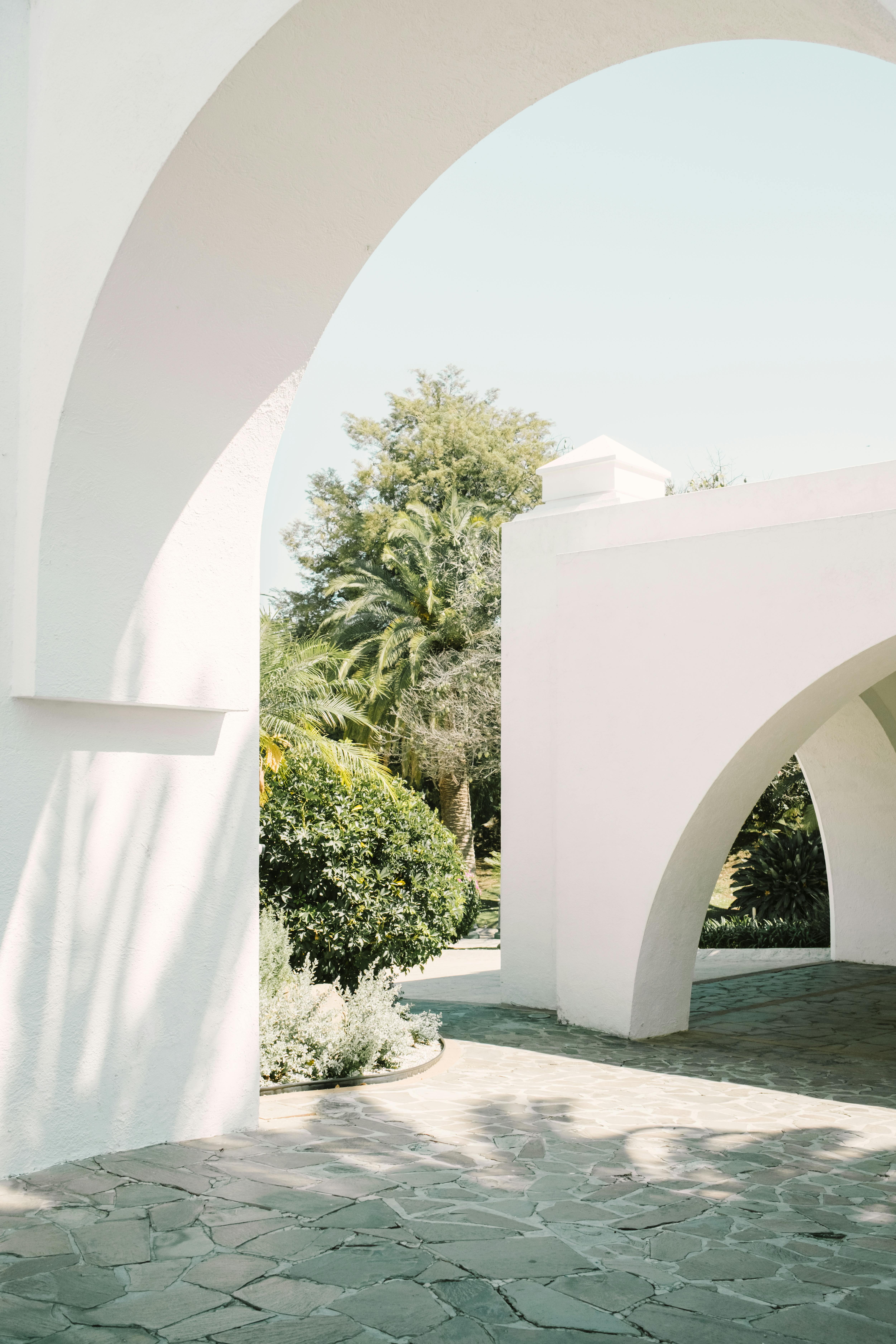Bright Mediterranean-style courtyard with arches and greenery on a sunny day.