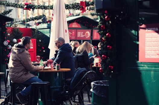 Outdoor holiday market scene with people dining, festive decorations, and a cheerful ambiance.