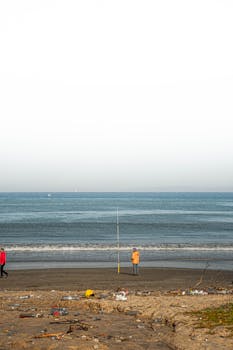 Fisherman standing by the sea on a peaceful day with clear skies, capturing a serene beach vibe.