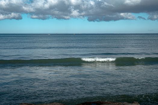 A serene ocean scene with gentle waves and a cloudy sky on a calm day.