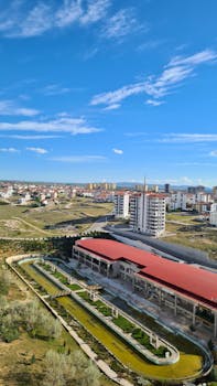Photo by Hicran Çabuk Aerial view of a modern cityscape featuring buildings and a landscaped park on a sunny day.