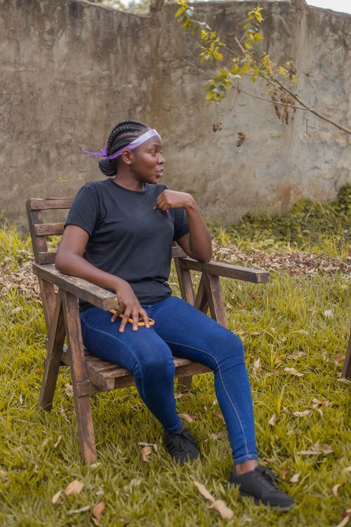 Free A woman sits relaxed in a wooden chair outdoors, surrounded by greenery. Stock Photo