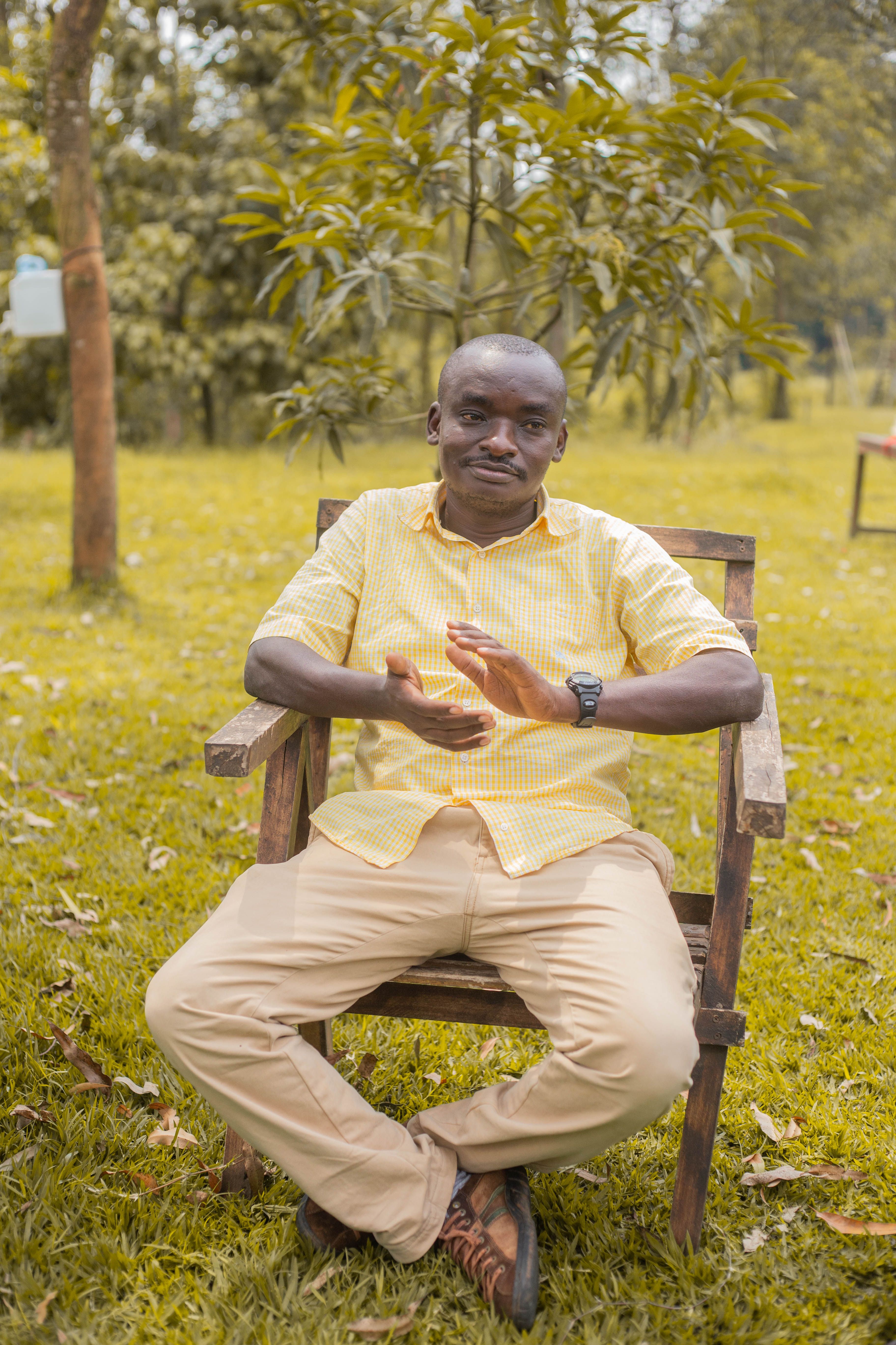 Portrait of a man sitting outdoors on a wooden chair in a garden setting. Bright and serene atmosphere.