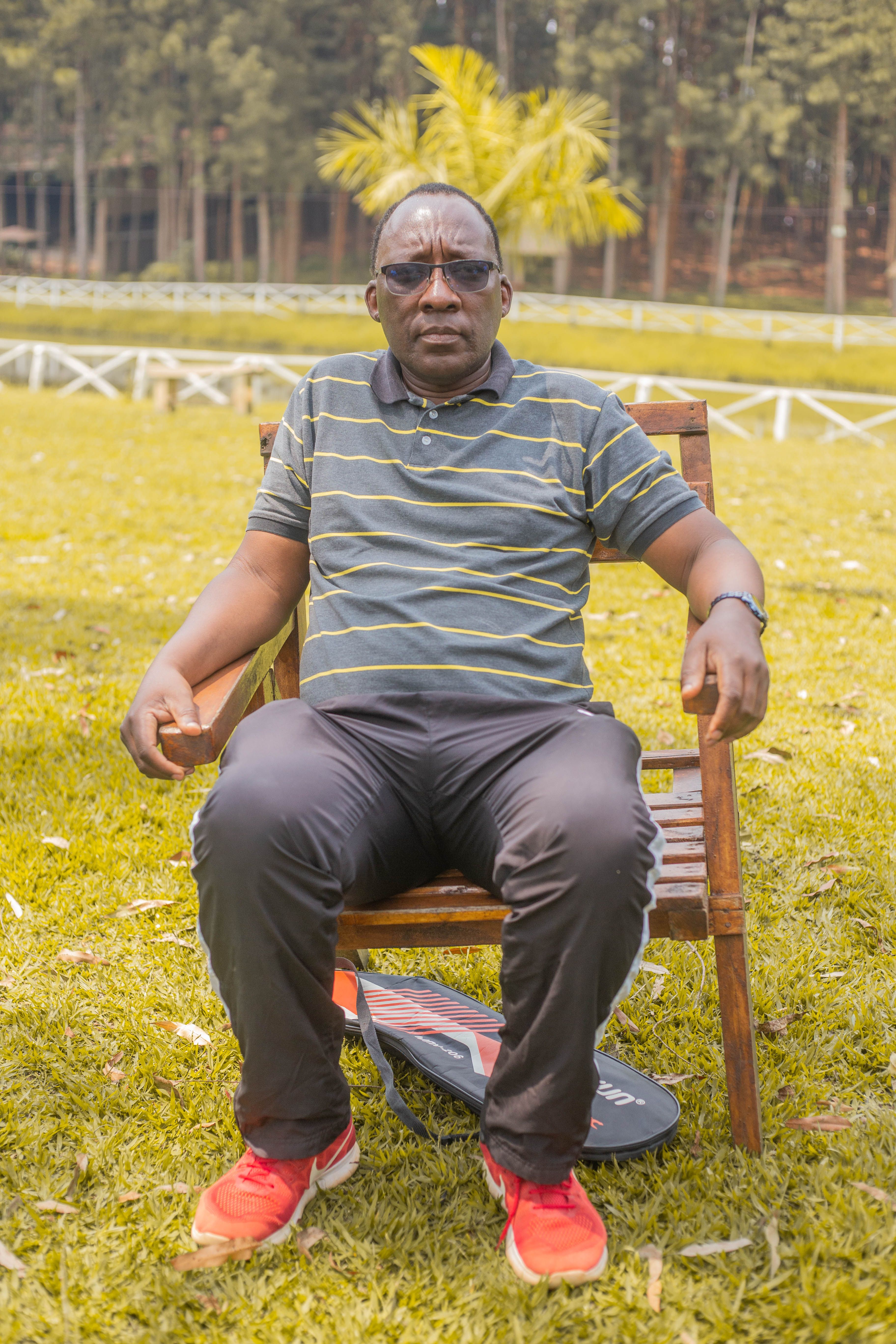Man enjoying a relaxing day outdoors in a park setting, sitting on a wooden chair.