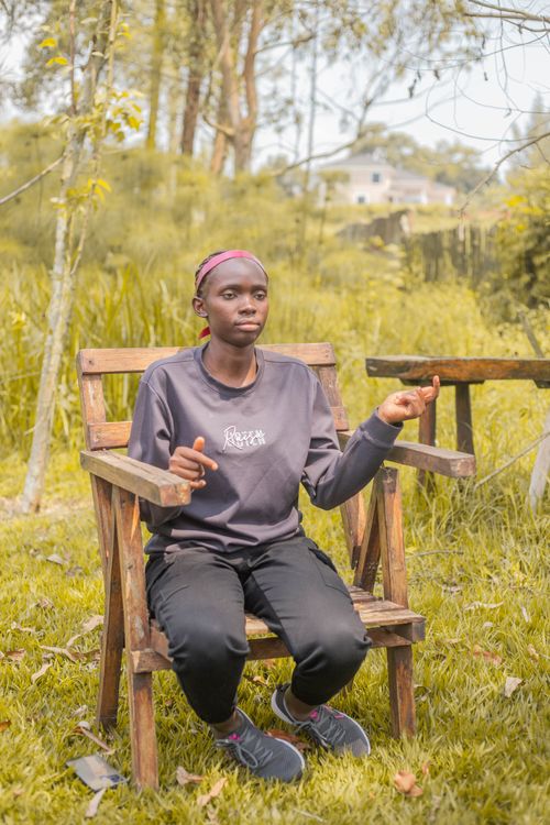 Free Individual wearing casual clothing seated on a wooden chair in a lush outdoor setting. Stock Photo
