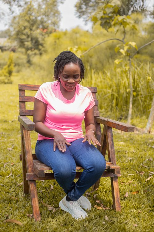Free A woman in pink sitting on a wooden chair outdoors, enjoying a sunny day. Stock Photo