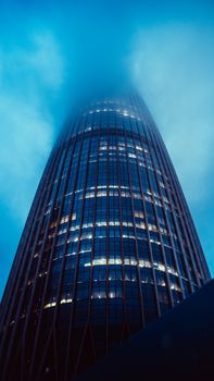 A striking skyscraper disappearing into misty clouds, creating a dramatic and moody cityscape.