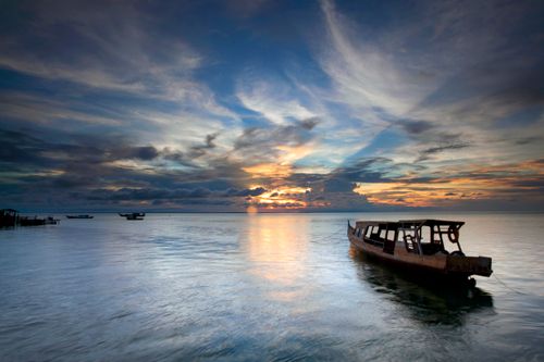 Free A serene sunset over the sea with a rustic boat, creating a tranquil and peaceful scene. Stock Photo