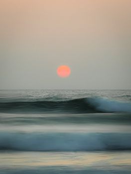 A peaceful scene of the sun setting over a calm ocean, creating a tranquil atmosphere with gentle waves.