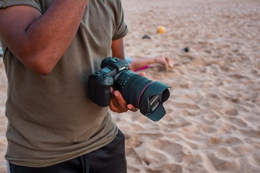 From above of crop unrecognizable man with modern digital photo camera standing on sandy shore during summer trip