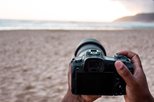 Photographer holding DSLR camera capturing a stunning beach sunset scene.