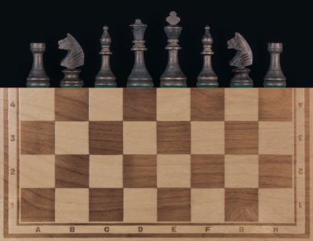 Top view of a wooden chessboard with vintage chess pieces on a black background.