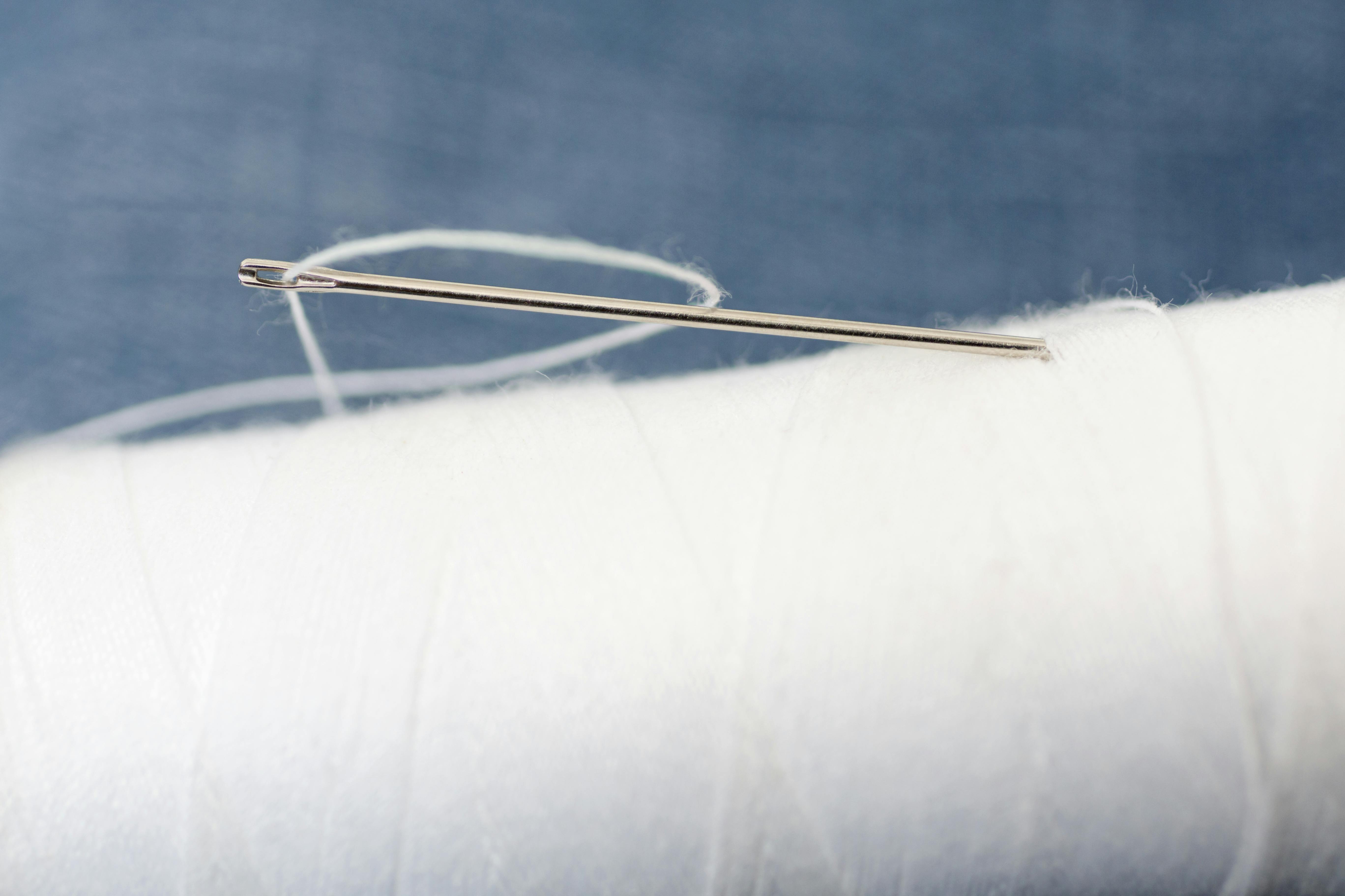 Detailed macro image of a sewing needle with white thread on a spool, perfect for crafting and tailoring concepts.
