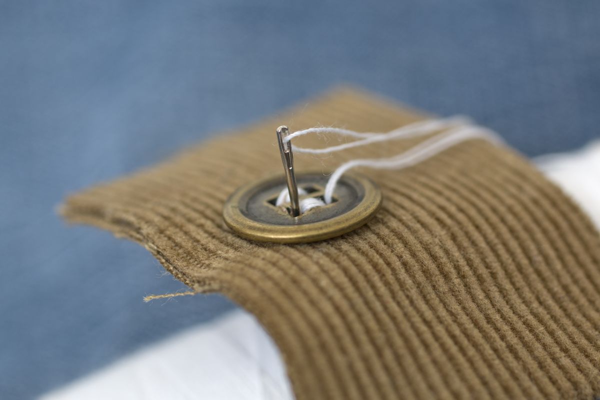 Needle threading a button onto corduroy fabric in a macro view