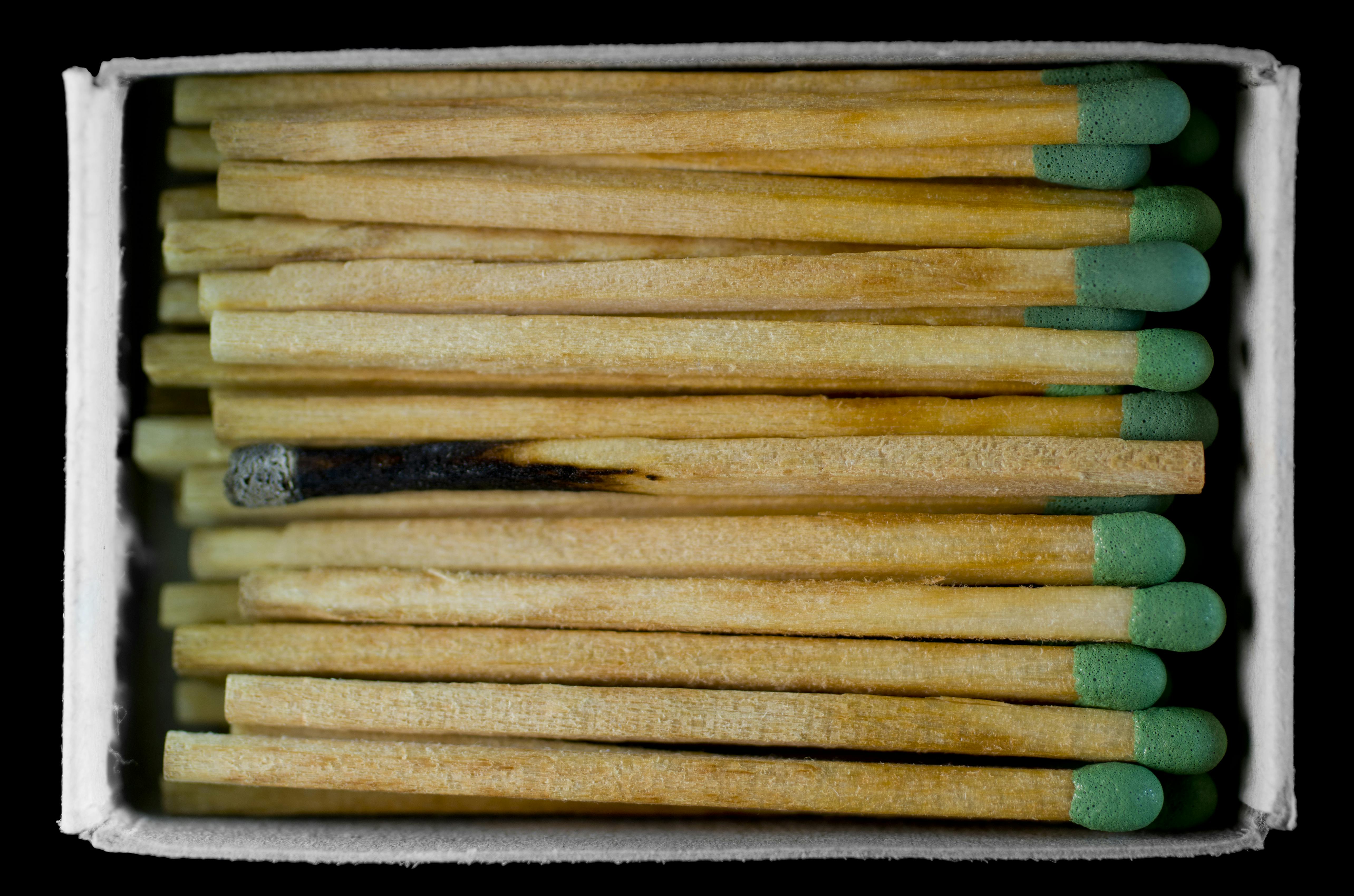 A stack of matches in a box viewed from above, featuring one burnt match among the unused ones.