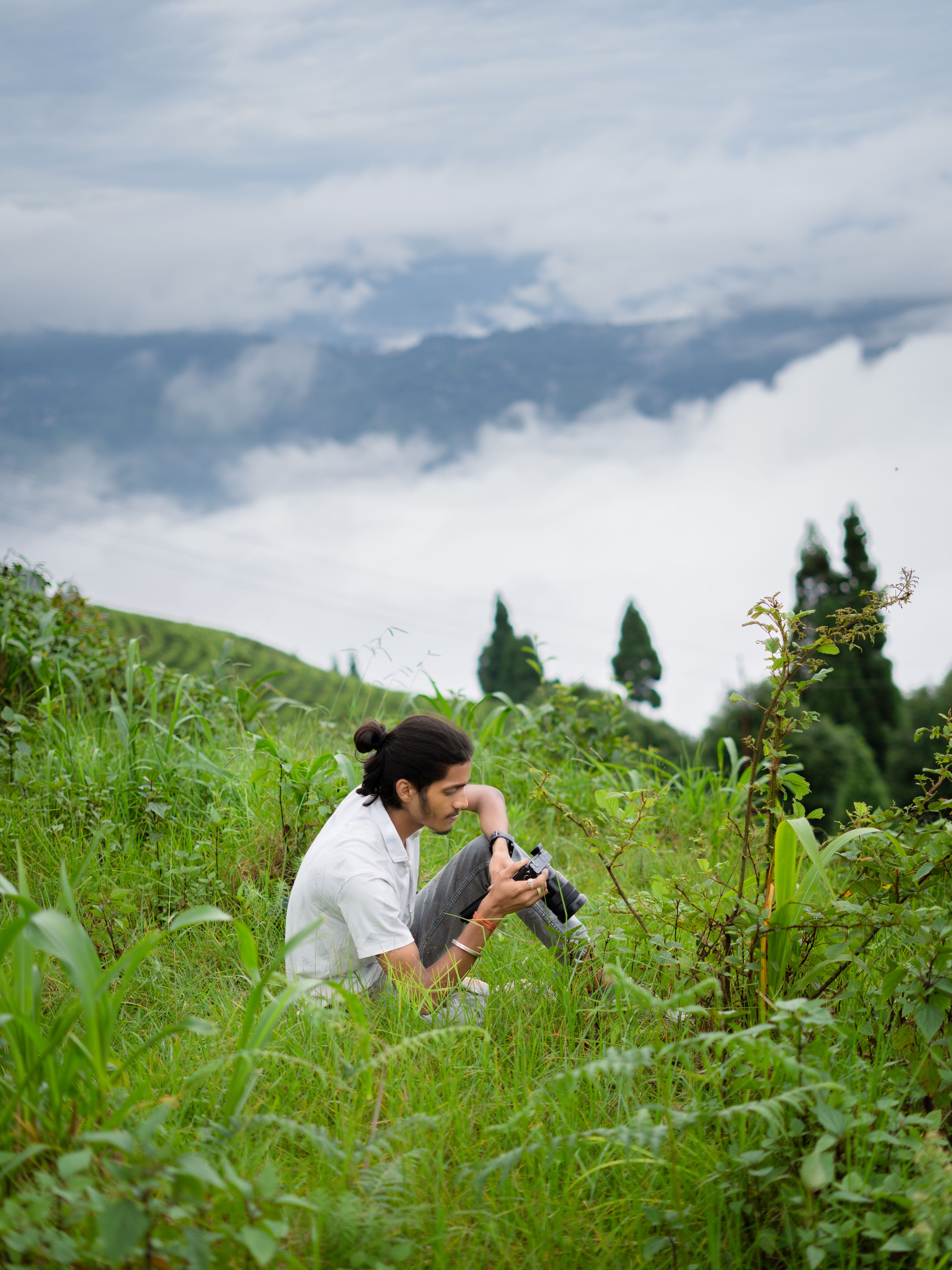 A young male photographer captures scenic views on a misty hillside, surrounded by lush greenery.