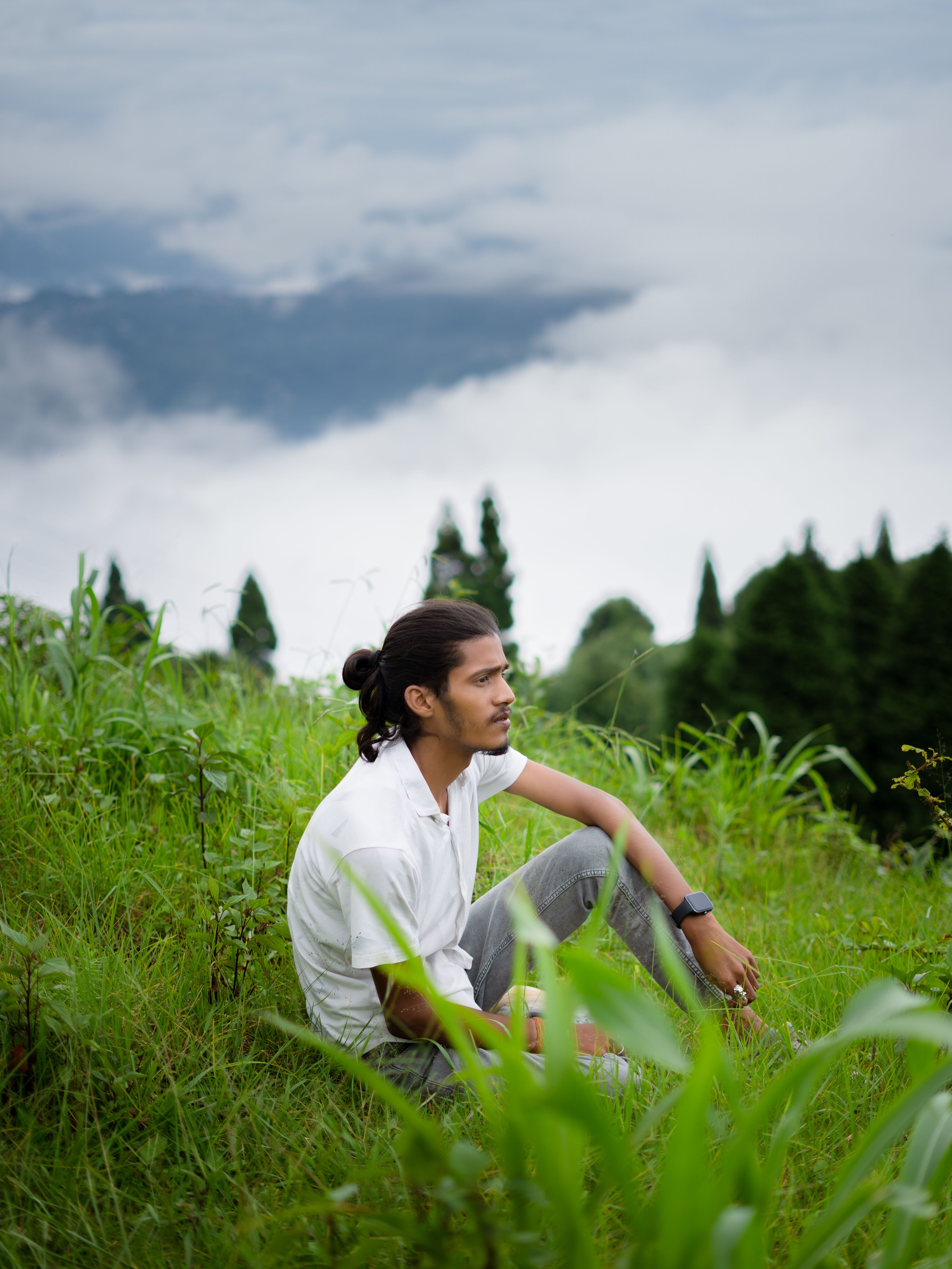 Young man in white shirt enjoying serene mountain landscape with cloudy sky.