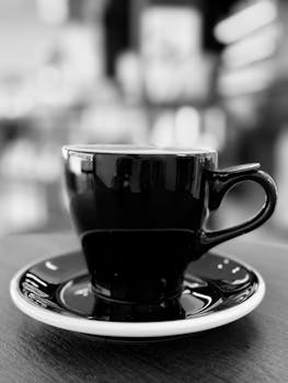 Black coffee cup and saucer, blurred café background, black and white.