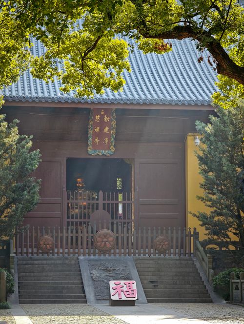 Free A serene view of an Asian temple entrance surrounded by lush trees under bright sunlight. Stock Photo