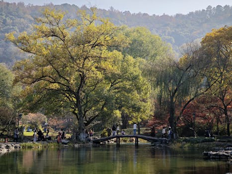 A tranquil park setting with people on a bridge, surrounded by colorful autumn foliage.