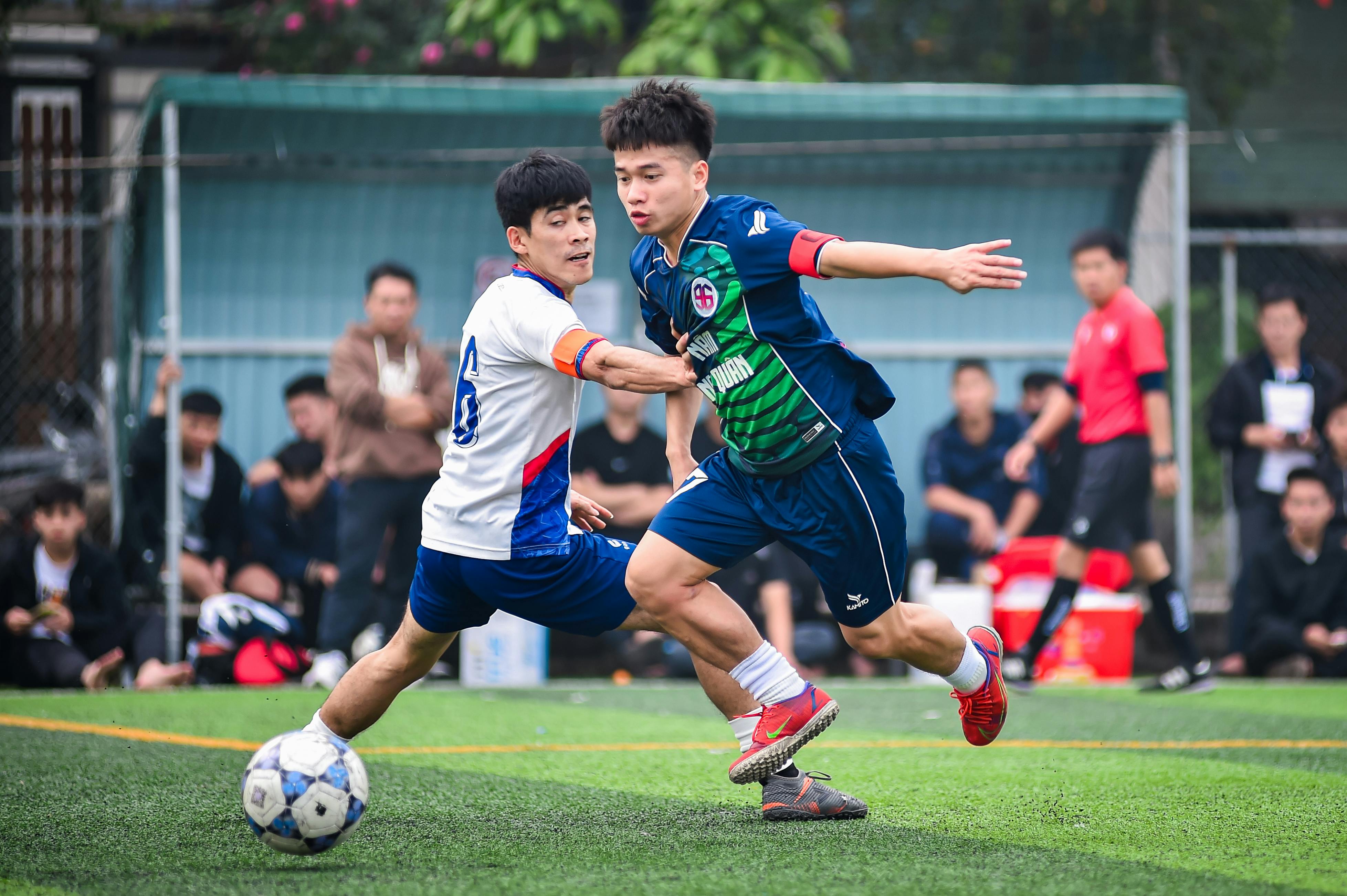 Two soccer players engaging in an intense match on a grassy field in Hanoi, showcasing athleticism and teamwork.
